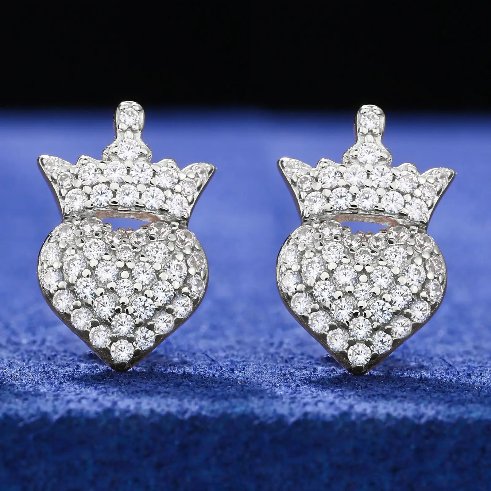 White gold 925 sterling silver moissanite crown heart stud earrings full display on blue table — showcasing crown-heart design, moissanite sparkle, 925 silver craftsmanship
