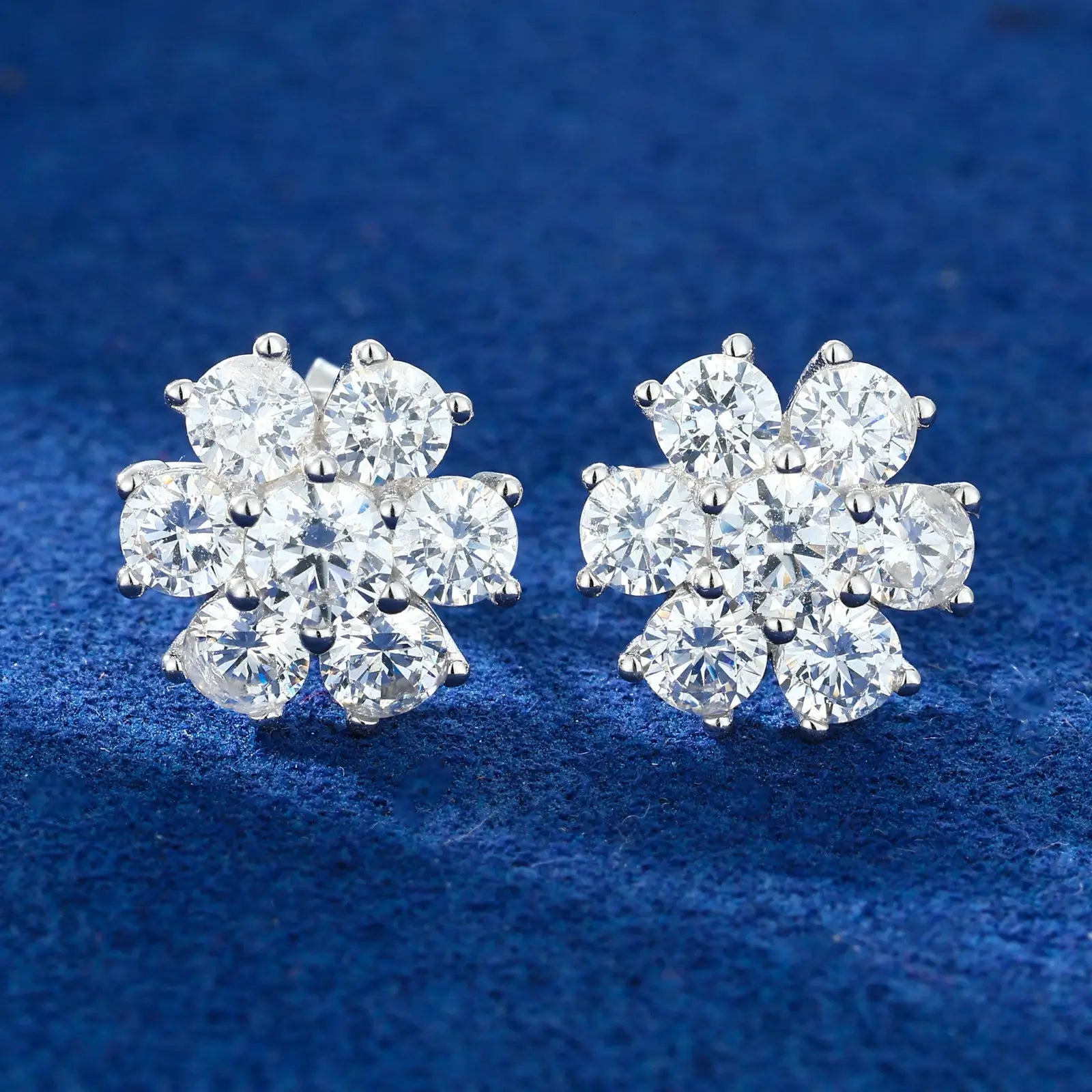 White gold 925 sterling silver moissanite radiance flower stud earrings full display on blue table — showcasing floral design, moissanite sparkle, 925 silver craftsmanship