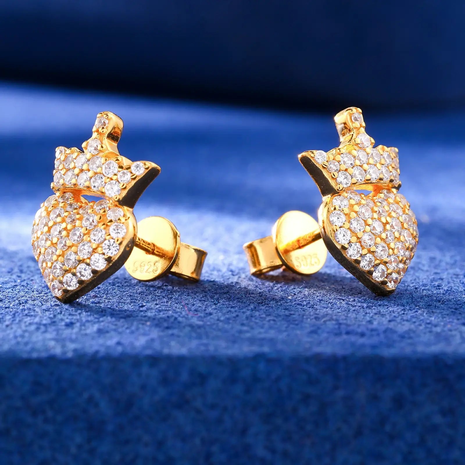 Side close-up of yellow gold 925 sterling silver moissanite crown heart stud earring on blue table — highlighting moissanite detailing, crown-heart texture, 925 silver build