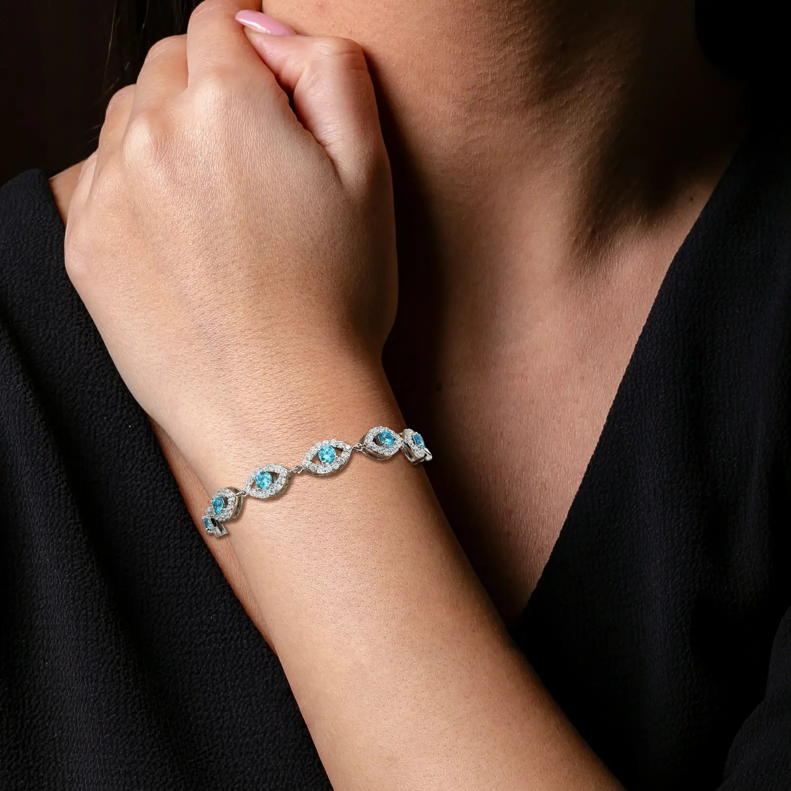 Caucasian woman stacking blue center evil eye bracelet with other chains - lab-grown moissanite scattering spectral rainbows | Waterproof spiritual stack