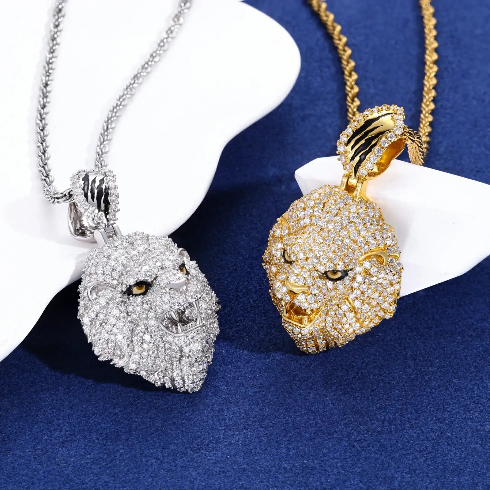 Gold and white gold lion head pendants displayed back-to-back on blue table - comparing finishes and moissanite brilliance