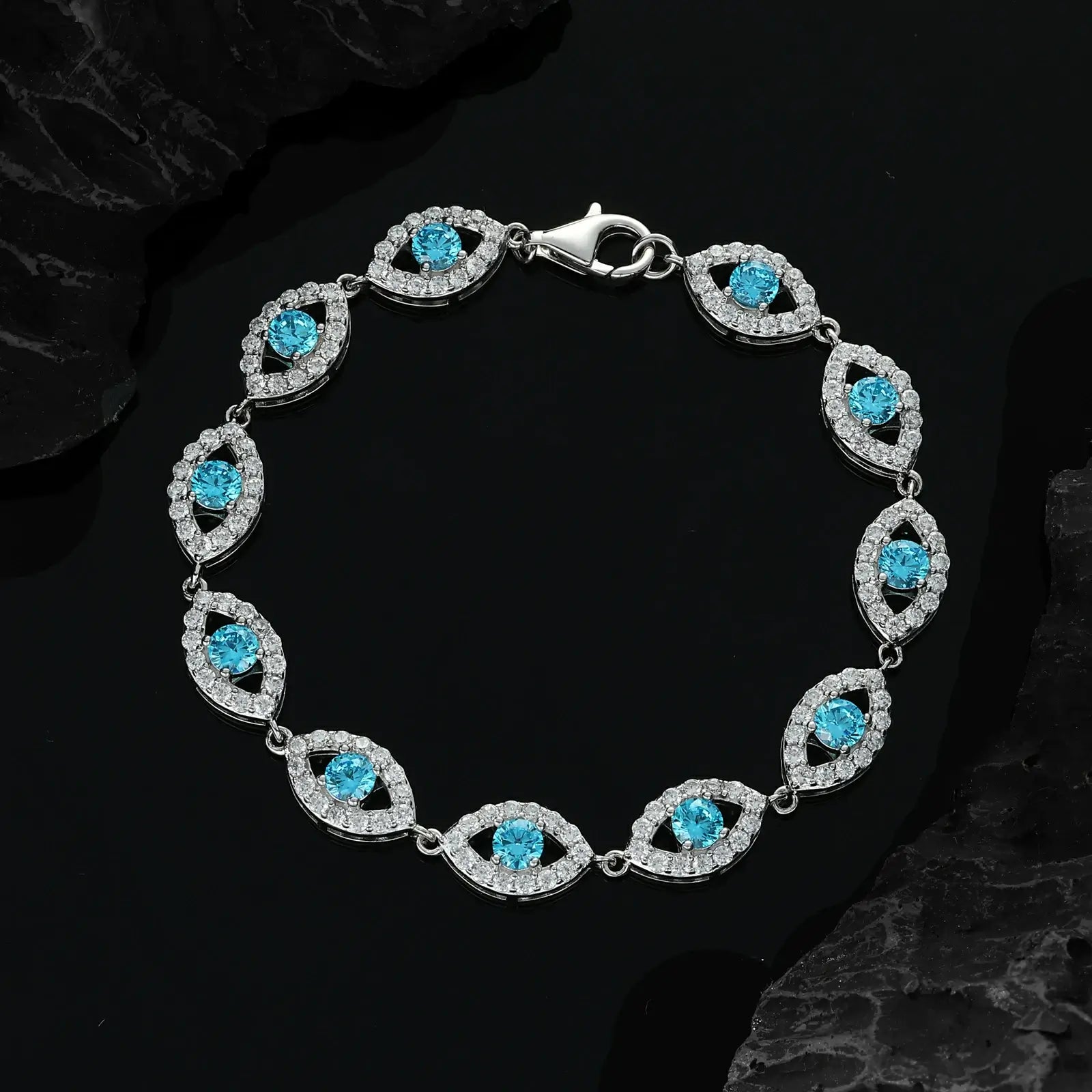 Top-down view: White gold evil eye bracelet on marble - blue center moissanite blazing cerulean fire | ISO 3160-2 waterproof certified