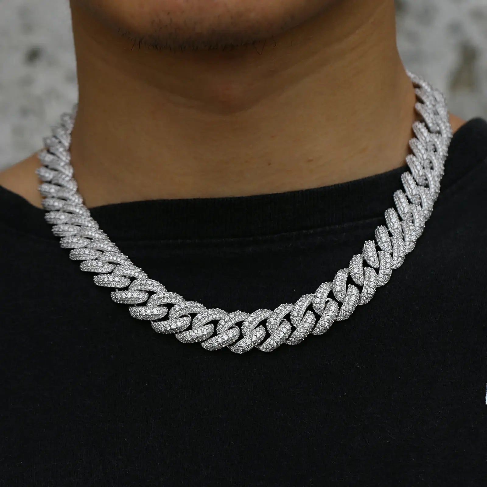 Confident man wearing a 15mm white gold Cuban link chain with three rows of moissanite stones in a stylish urban setting, perfect for casual or formal outfits.