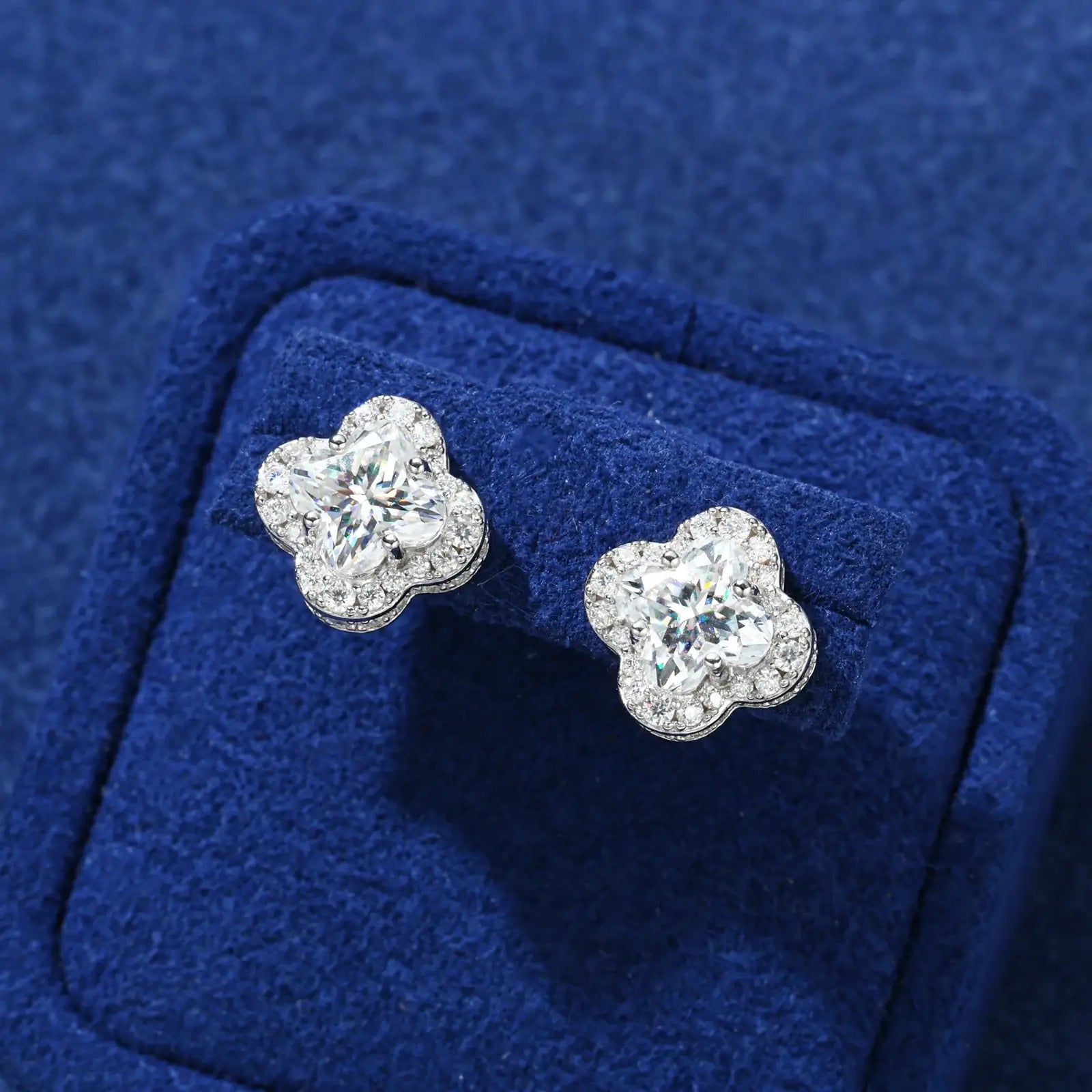 Front close-up of white gold 925 sterling silver lily cut moissanite four leaf clover stud earring on blue table — highlighting lily-cut moissanite brilliance, clover petal details, 925 silver build