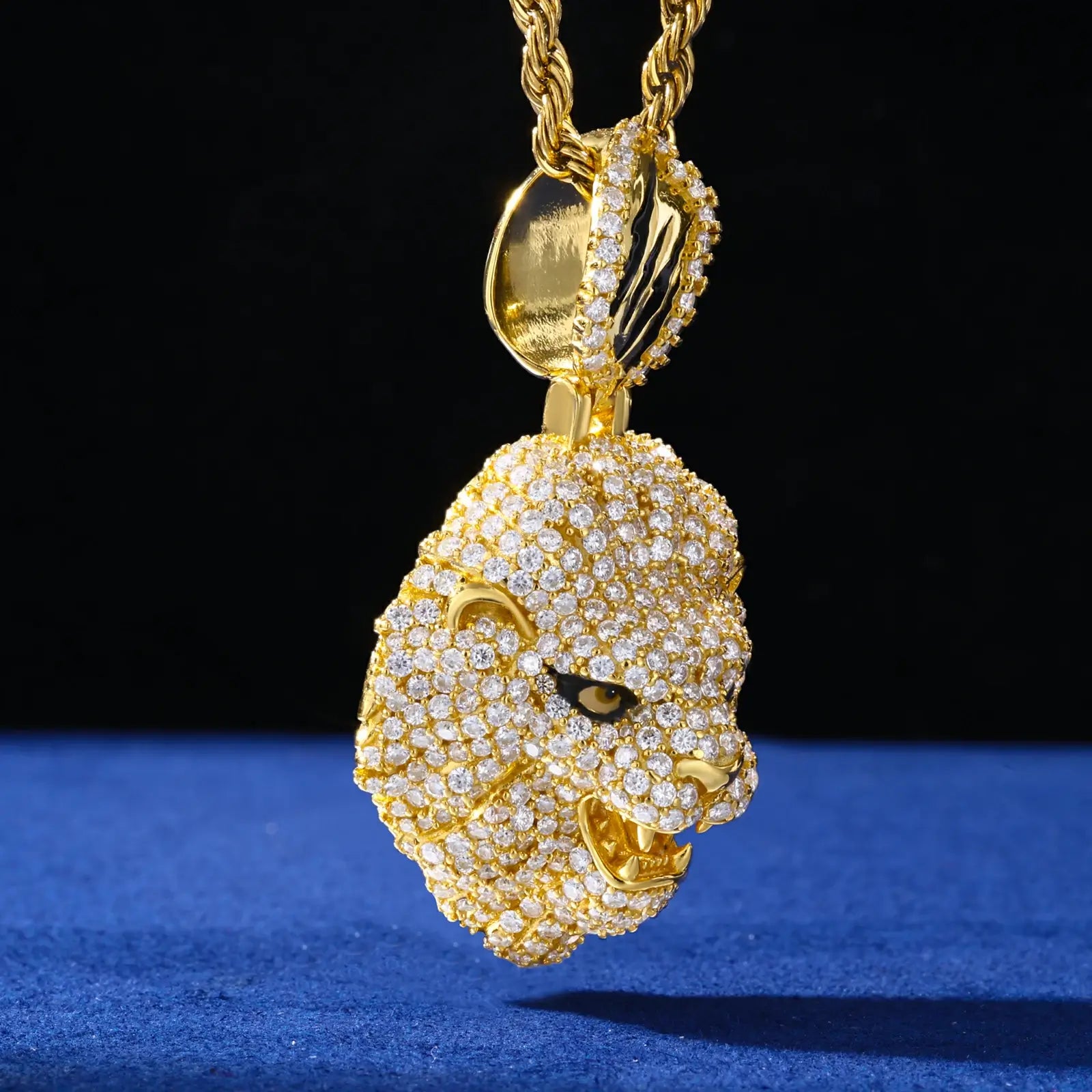 Side view of gold lion head pendant hanging on blue table - showing 3D construction and micro pave stone setting