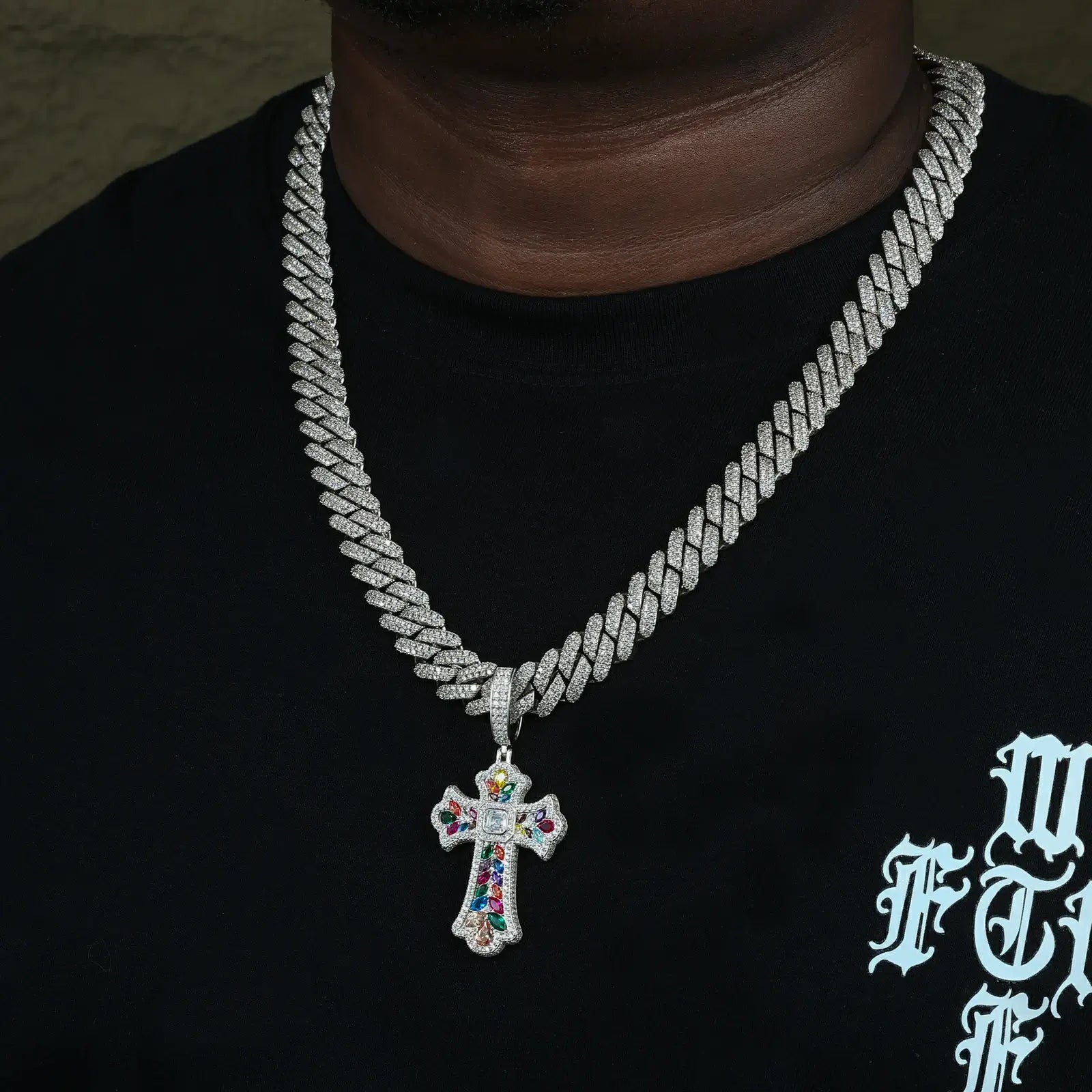 Unisex cross necklace for men in white gold finish, worn with graphic tee showing rainbow moissanite stones in daylight