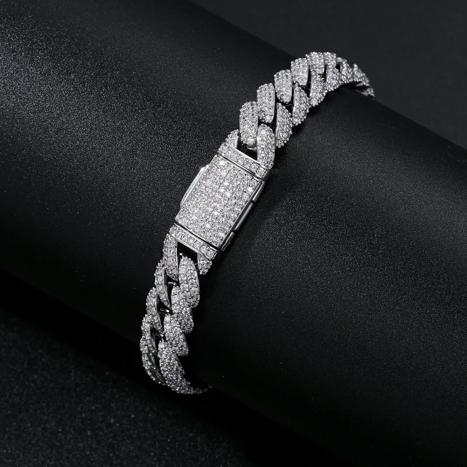 Detailed close-up of white gold Cuban bracelet clasp on black desk, featuring secure box closure and diamond-cut CZ stone setting.